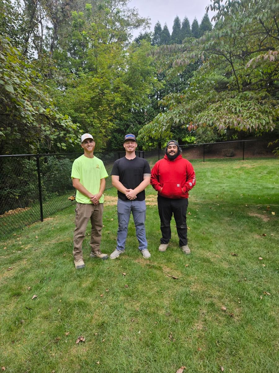 Chandler Usenicnik and two crew members standing in a backyard next to a new black chain-link fence