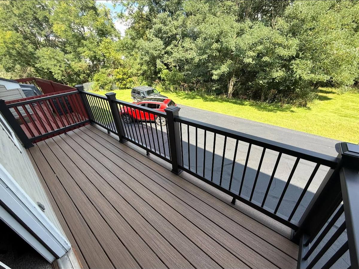 Brown composite deck with black aluminum railing overlooking a backyard