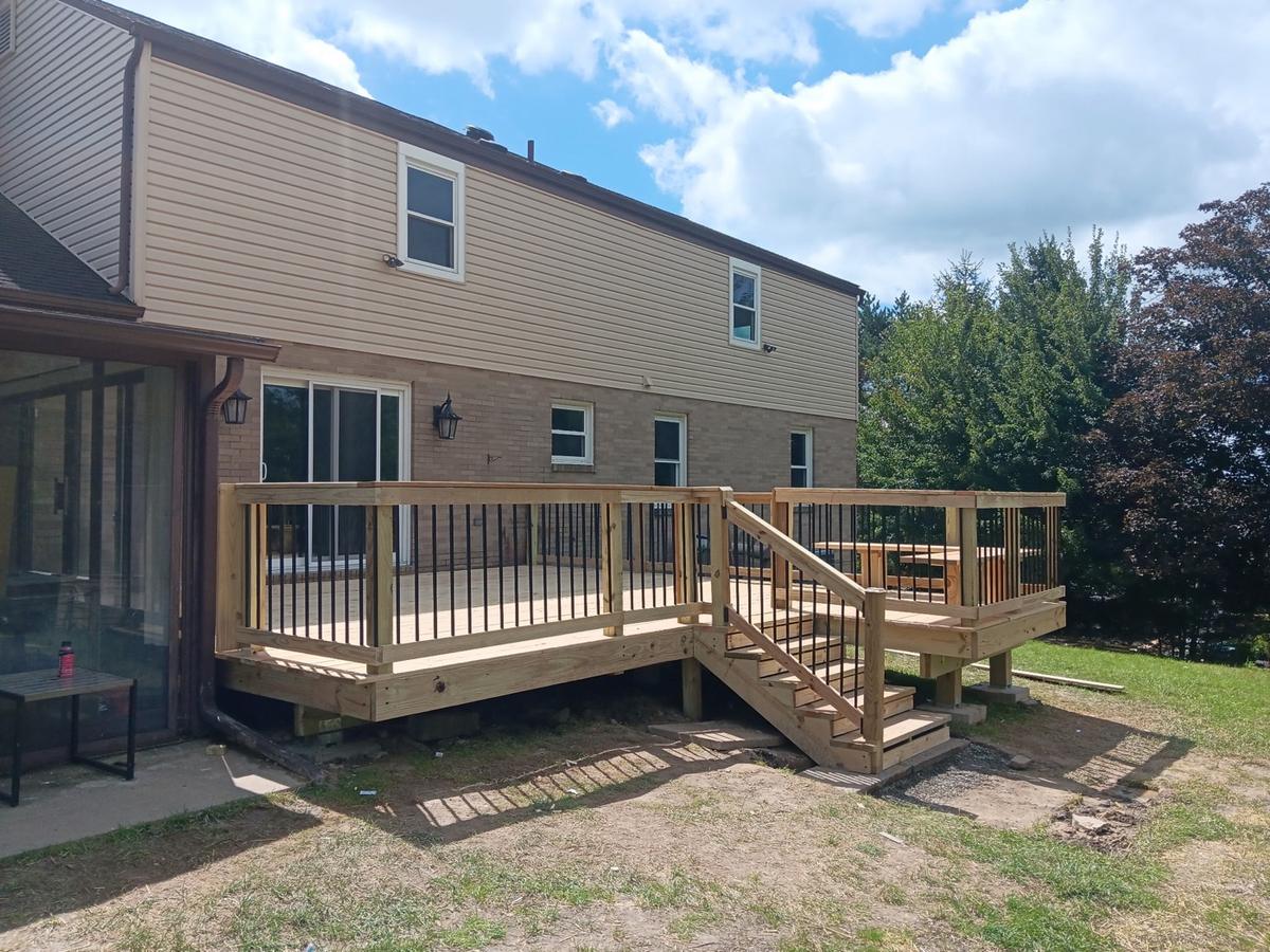 New pressure-treated wood deck with railings and stairs on the back of a two-story home