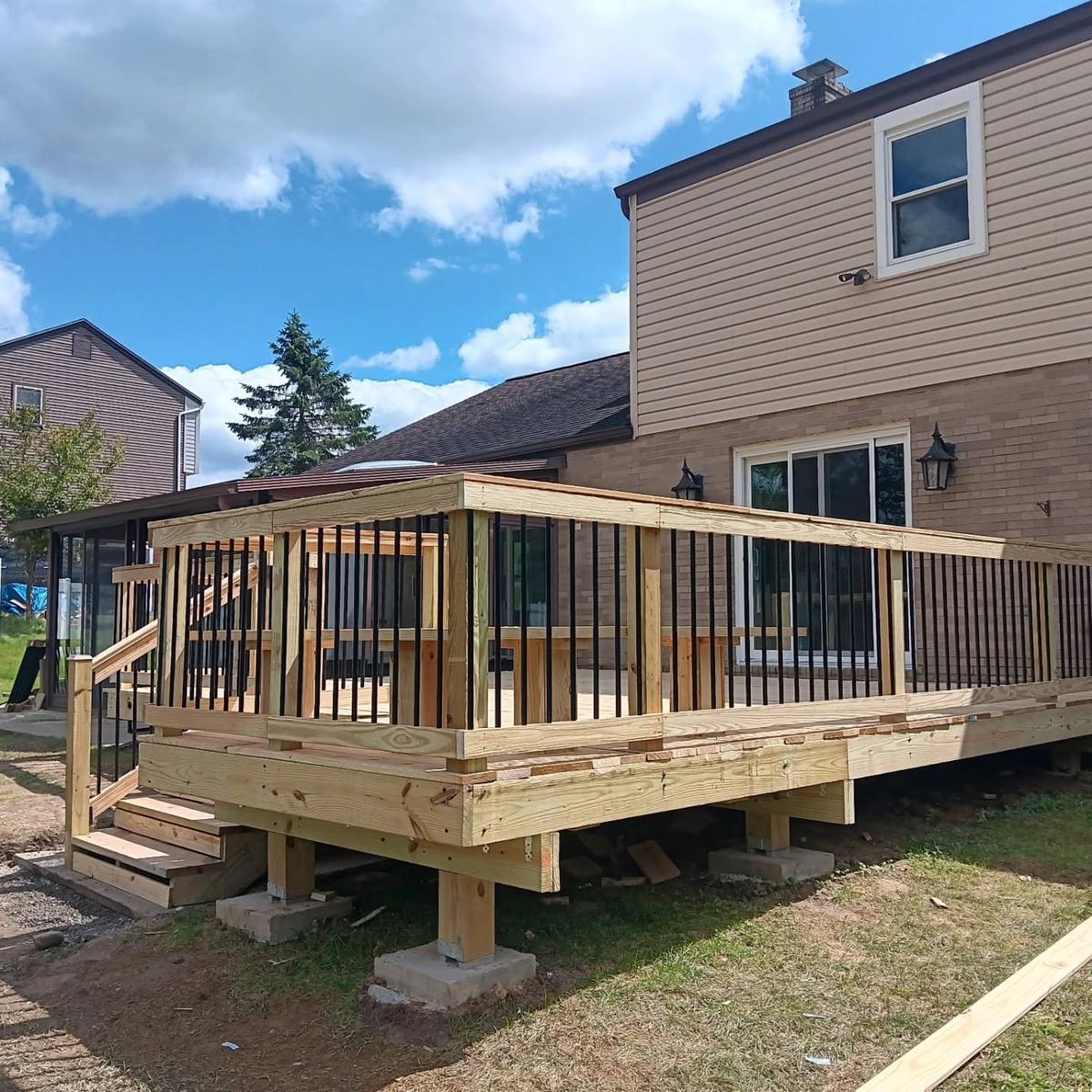 New raised pressure-treated deck with black balusters on the back of a two-story home