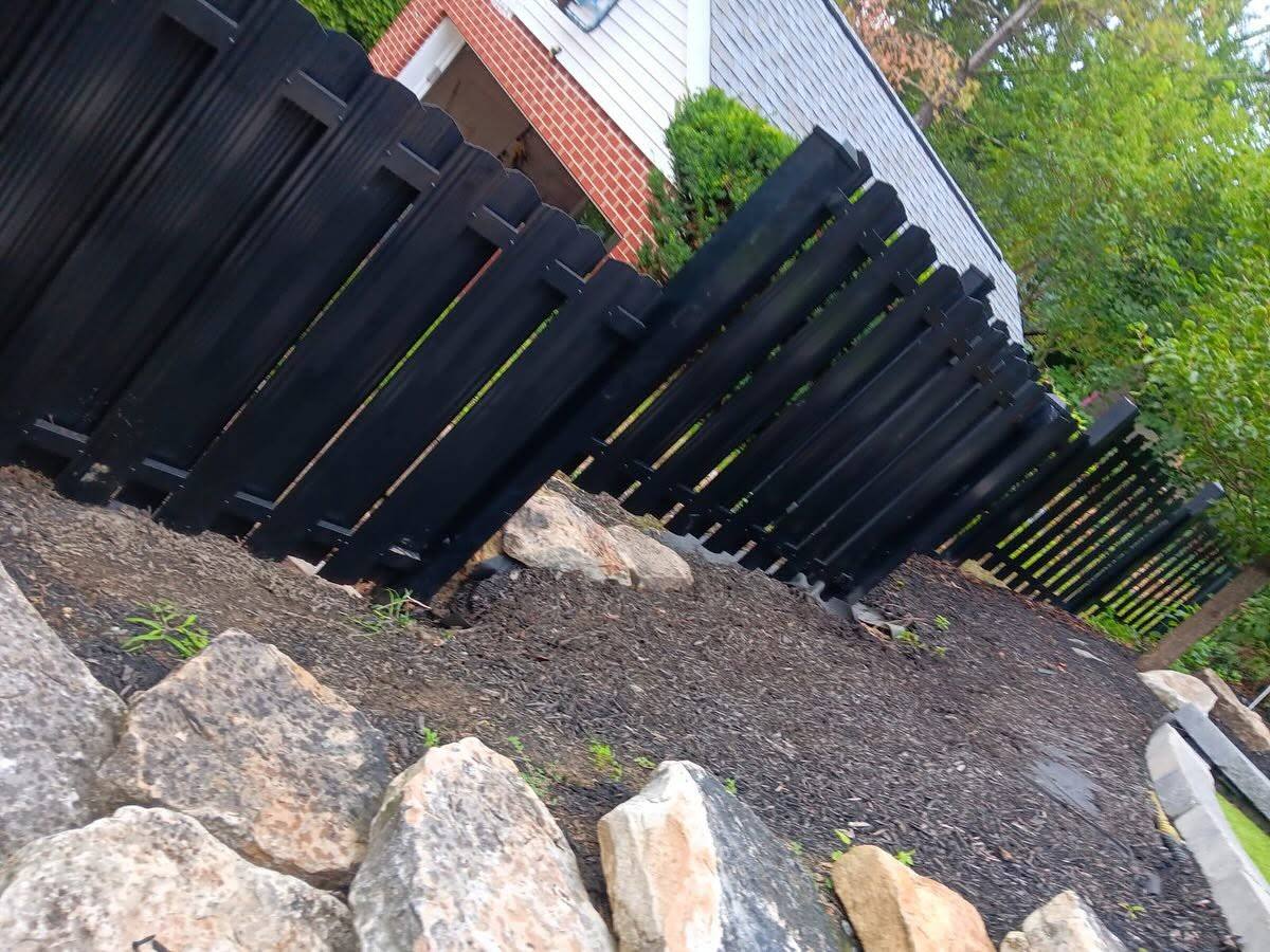 Black board fence stepping down a sloped yard above a rock border