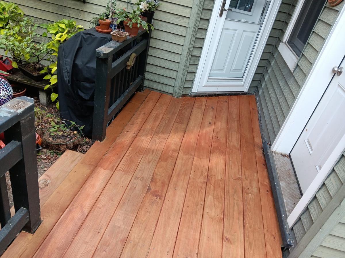 Freshly stained wood porch deck by a side door, with black railing